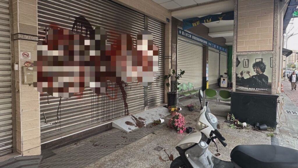 事發現場全景，店家鐵捲門留有大片漆痕，地上滿是遭毀損的植栽與雜物。